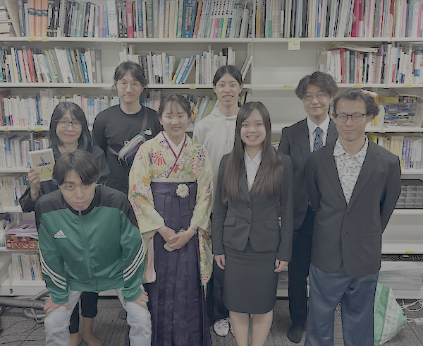 研究室の本棚の前に並ぶ先生と学生
